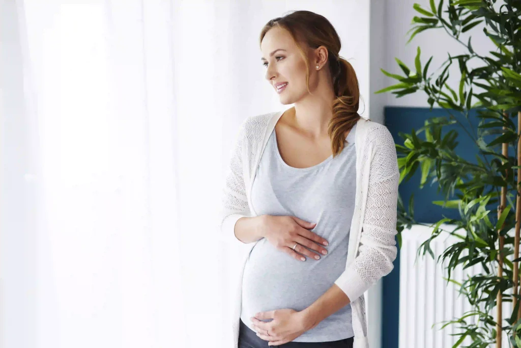 A happy and healthy pregnant woman looking out of a window.