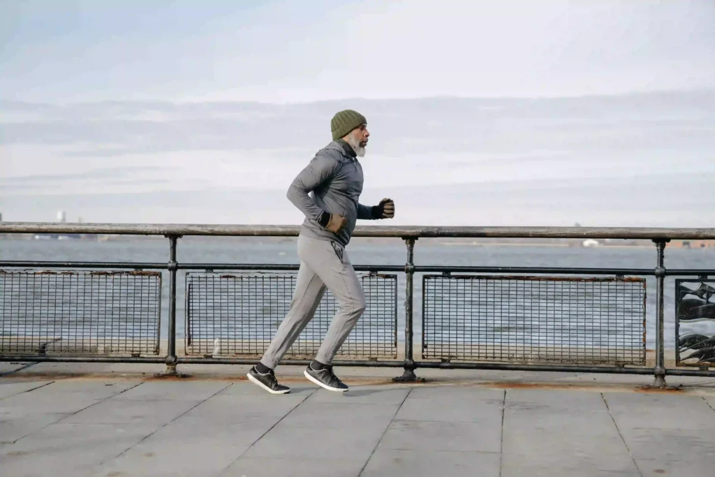 Healthy old man running on a pier with a grey sky.